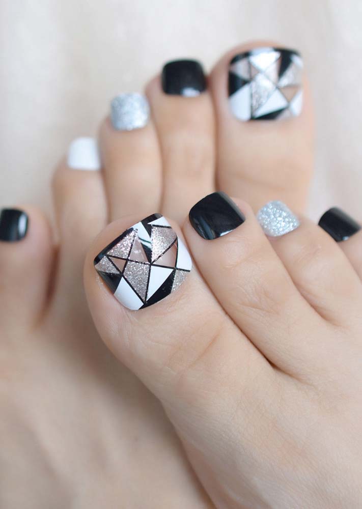 Francesinha preta e divisão em vários triângulos em preto, branco e prateado com glitter em destaque nessas unhas do pé decoradas.