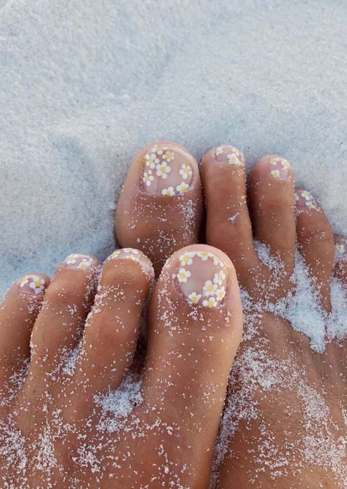 Delicadeza é a palavra certa para descrever essas unhas do pé decoradas com margaridas brancas com miolo amarelo distribuídas sobre a unha com base transparente.