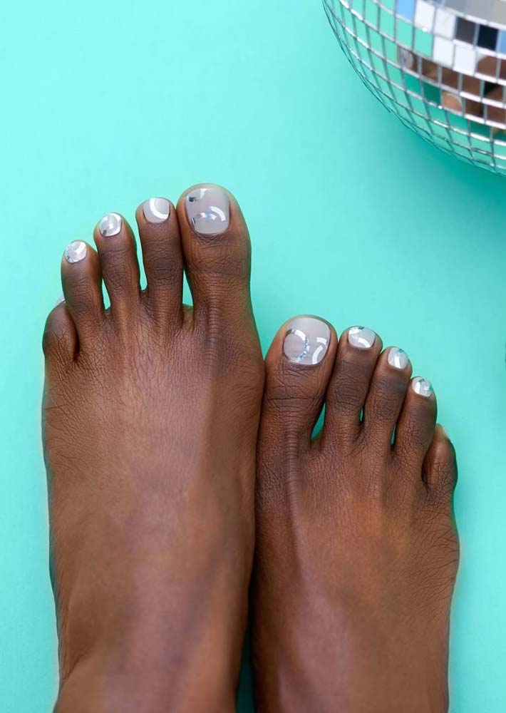 Outra ideia de unhas do pé decoradas simples: esmalte cinza claro no fundo e adesivos semicirculares prateados.