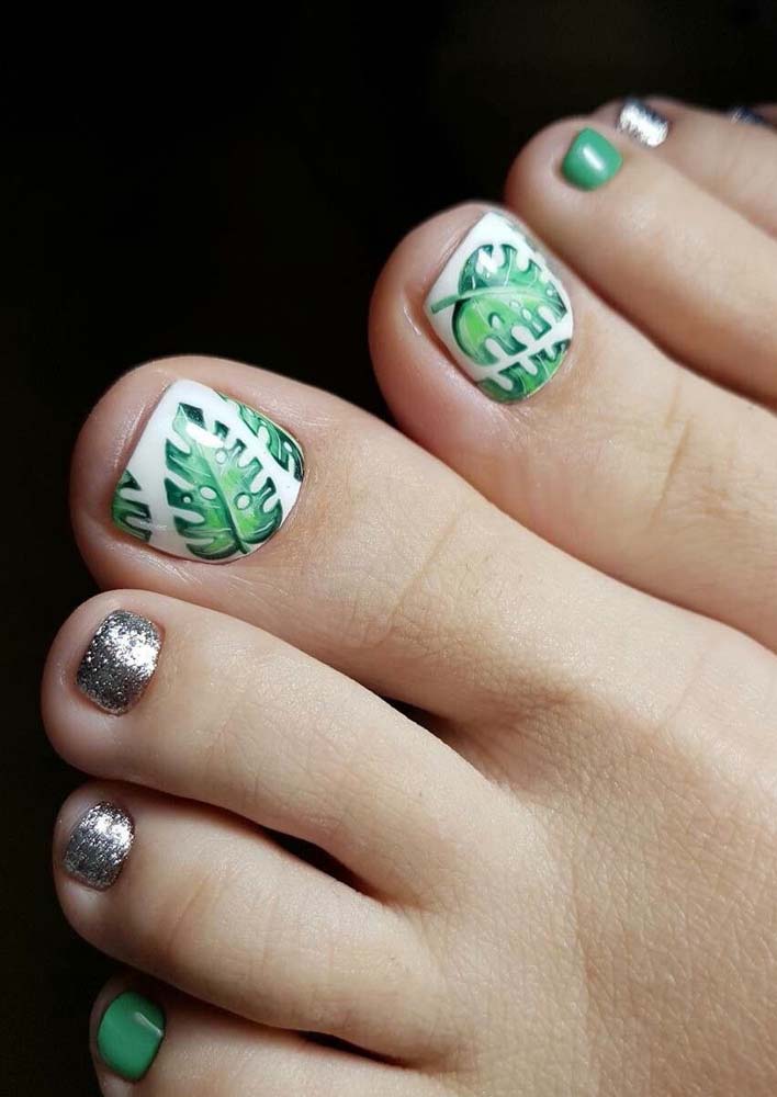 A folhagem exuberante da costela de adão no adesivo no dedão rouba toda a atenção nessas unhas do pé decoradas em verde e prateado com glitter.