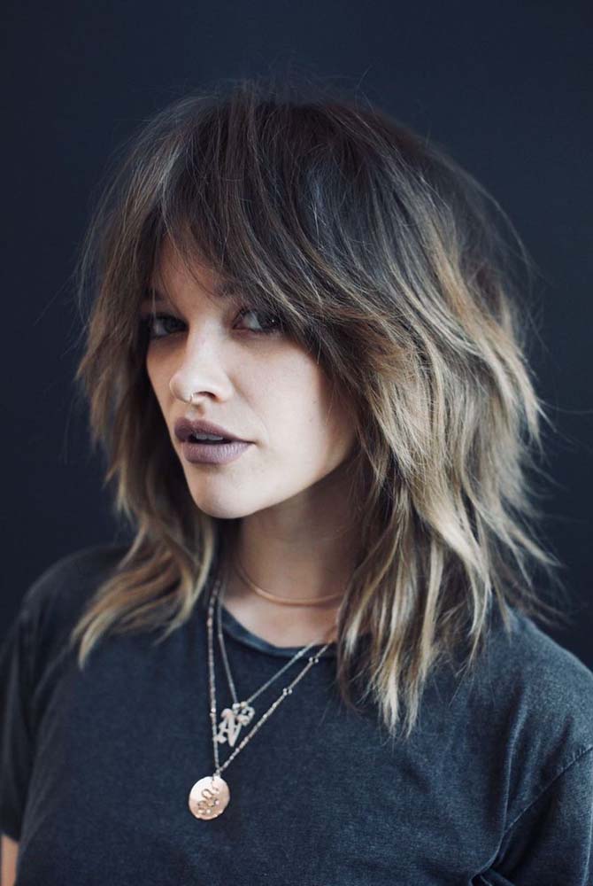 Corte em camadas, bem desfiado, com franja bardot e mechas peroladas no cabelo escuro: um visual rocker bem despojado, com inspiração direta nos anos 1980.