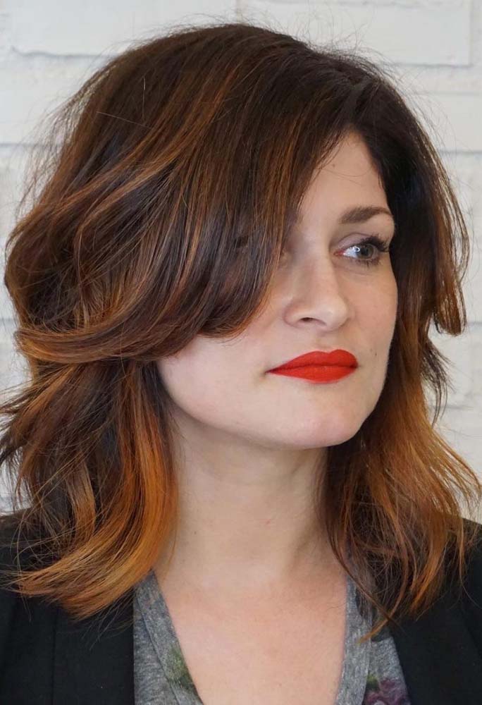 As mechas ruivas garante mais profundidade para esse cabelo long bob com franja lateral longa dividida ao meio.