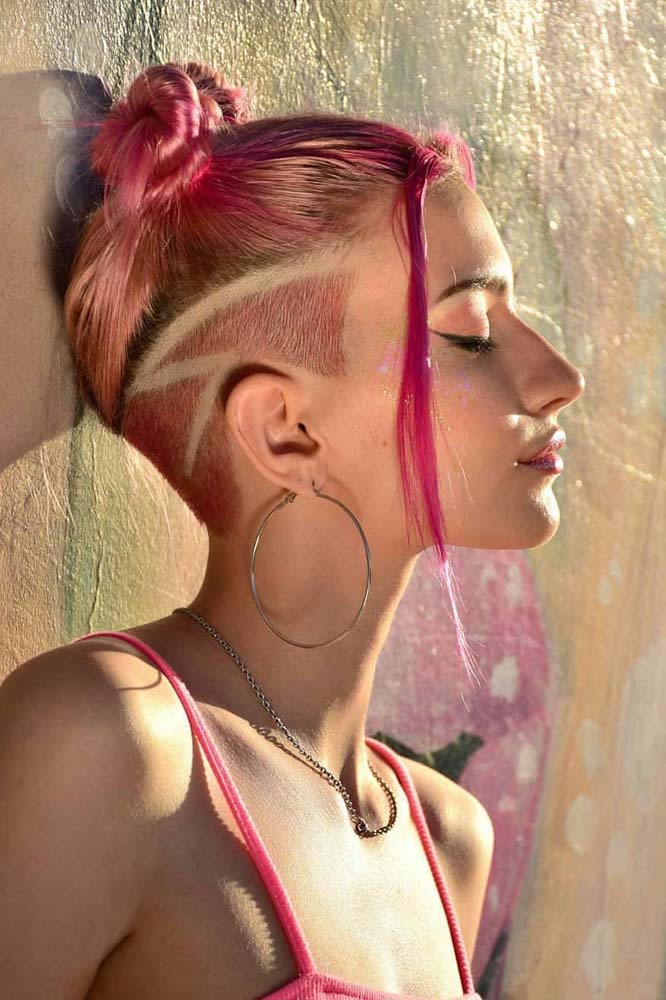 Visual de atitude e totalmente rosa com penteado double bun, mechas frontais soltinhas e undercut na nuca e laterais com um risco de raio.