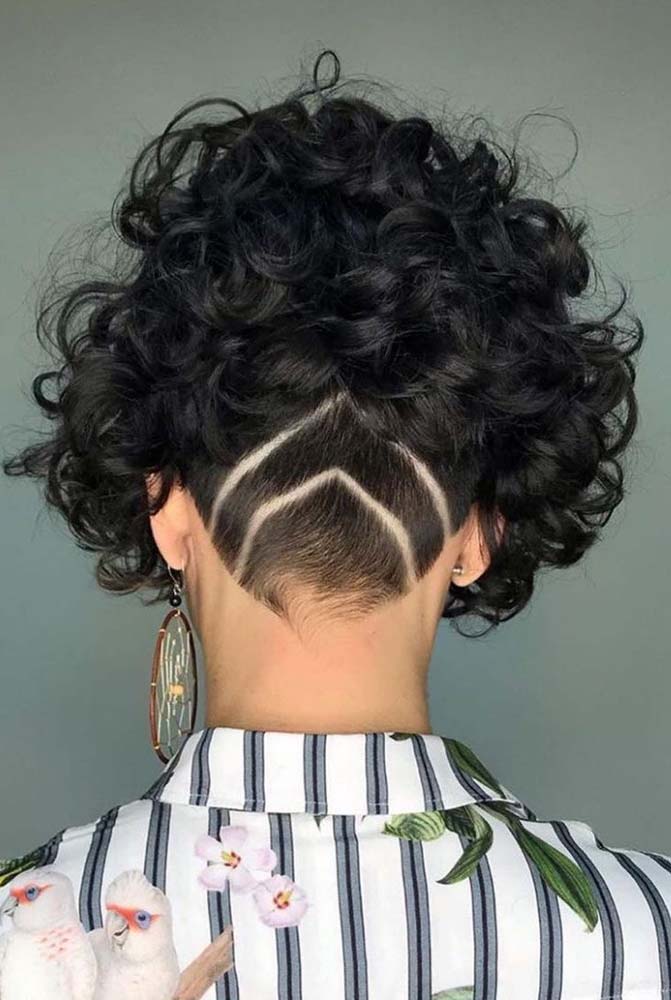 Nesse exemplo com cabelo cacheado curto, por outro lado, o undercut é feito com um pente maior da máquina, o que permite que as setas desenhadas com navalha fiquem mais aparentes.