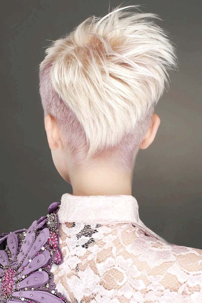 Cabelo com corte pixie assimétrico com um degradê diagonal no comprimento de trás, que cobre parcialmente o undercut que toma toda a nuca e as laterais do cabelo. 