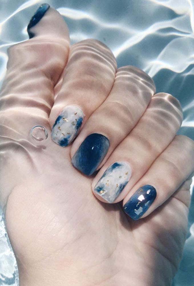 Unhas decoradas azul com branco com cada uma num efeito marmorizado diferente - os toques de dourado garante ainda mais elegância no visual.