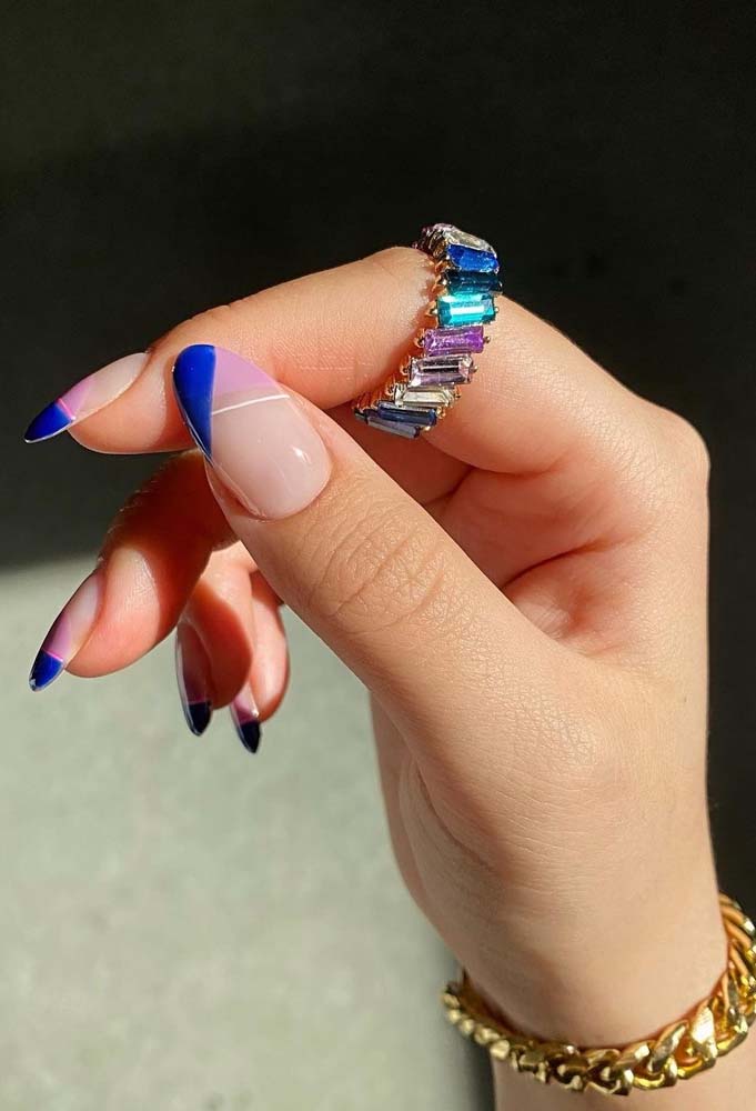 Azul royal só nas pontinhas das unhas em uma francesinha gráfica que também possui áreas lilás e linhas diagonais brancas fininhas.