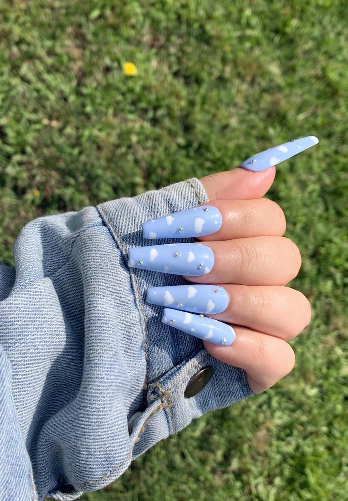 Nuvens branquinhas e estrelas feitas de strass por cima do tom clarinho de azul nessas unhas decoradas longas. 