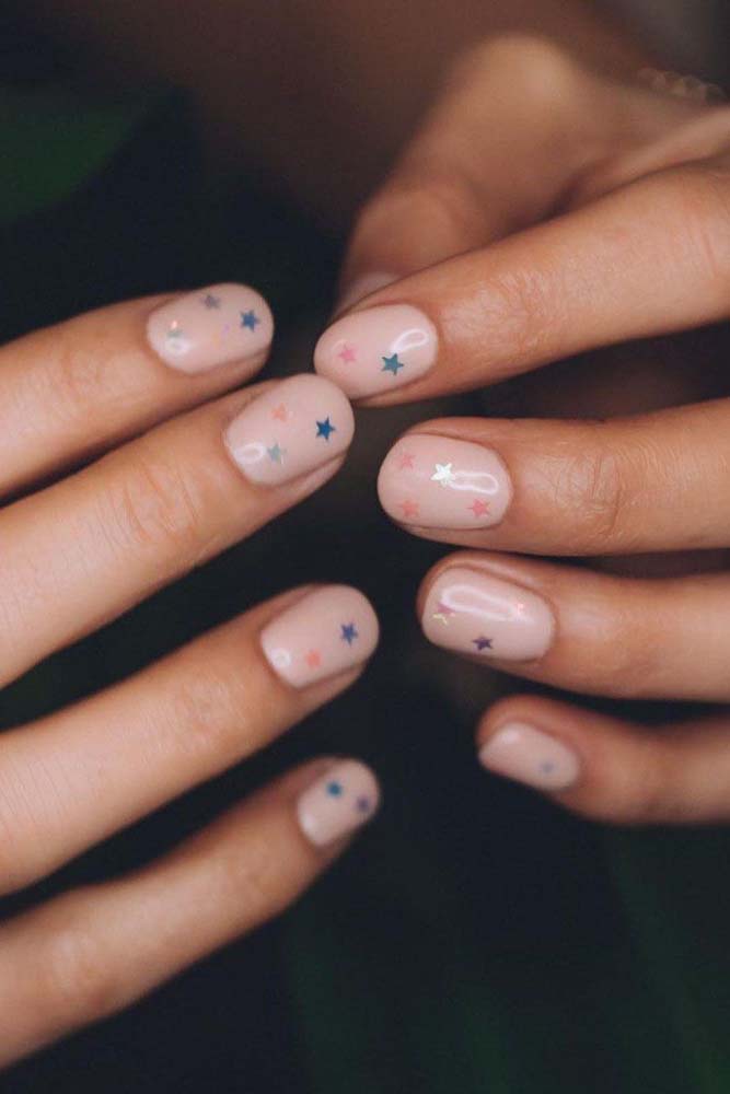 Unhas simples e bonitas com esmalte nude e delicadas estrelinhas coloridas