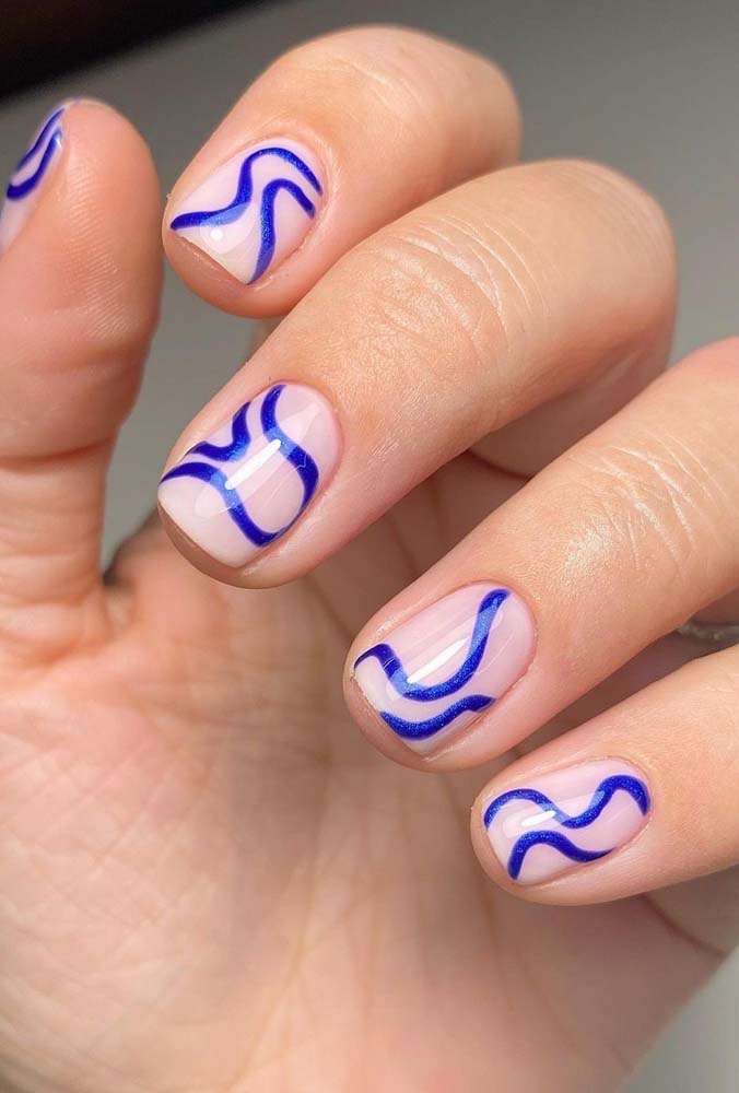 O esmalte nude dessas unhas redondas destaca a arte em azul