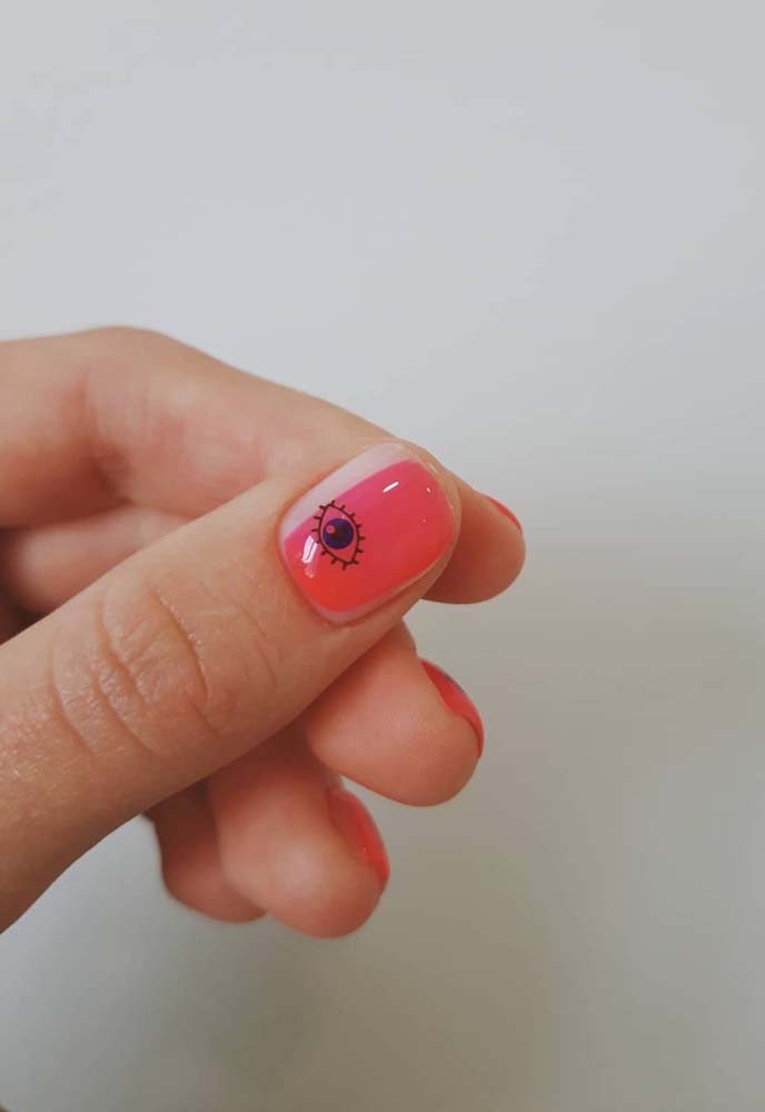 Assimétrica, essa esmaltação mescla vermelho com branco e um desenho de olho minimalista