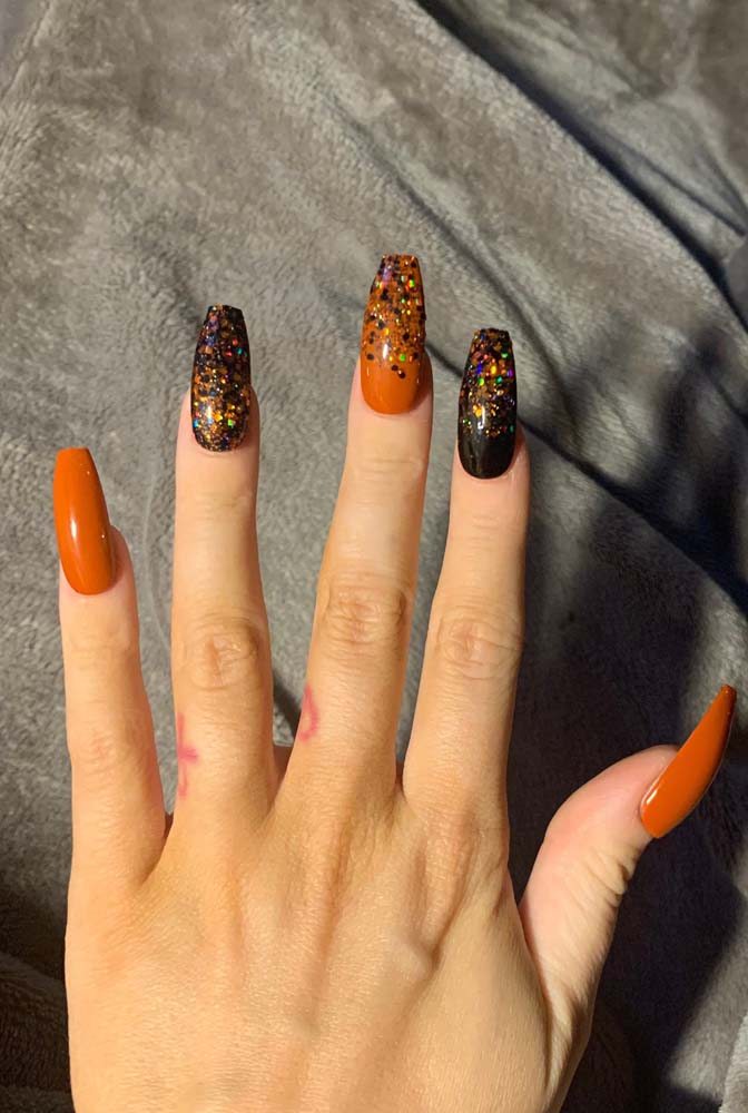 Esmalte preto e laranja. O glitter garante o efeito final para as unhas postiças decoradas